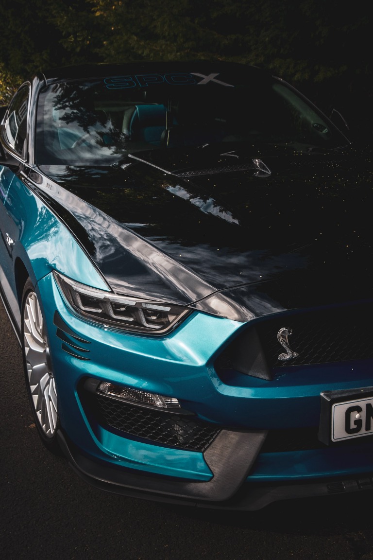Close-up of a turquoise performance car with a sculpted bonnet and cobra badge.