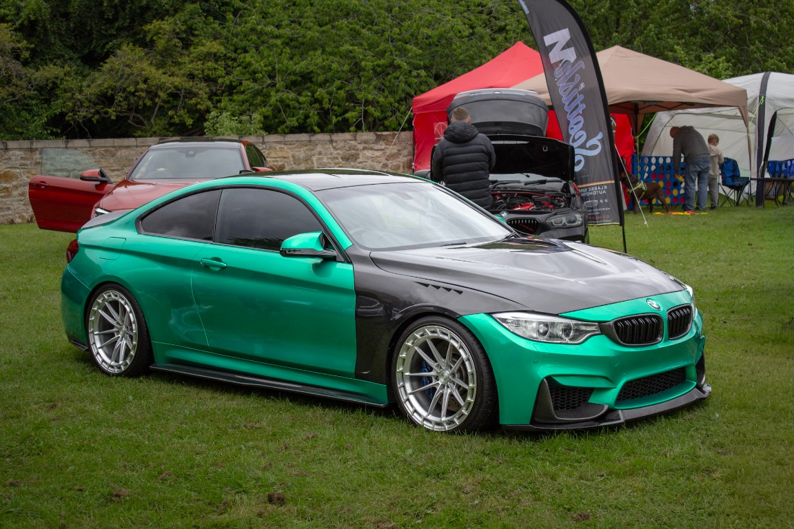 A green BMW coupe standing at a show with a crowd in the background.