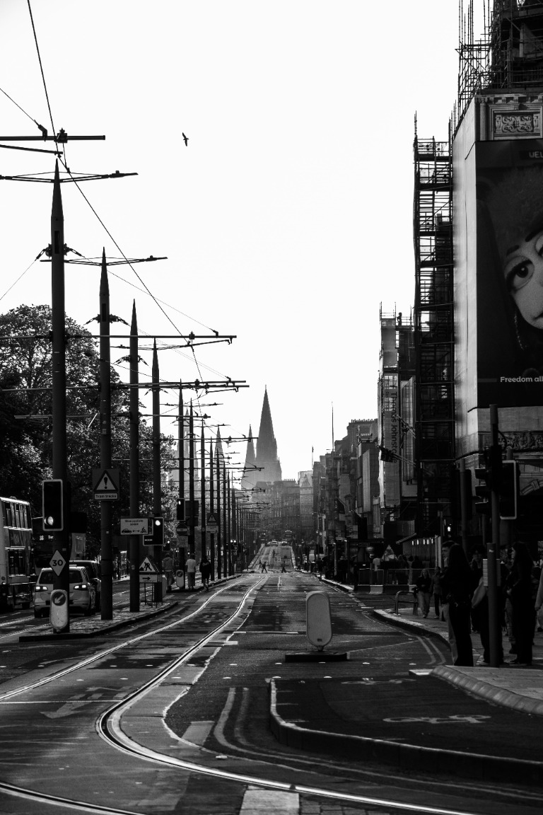 Black-and-white view down a city tram street, with a bird crossing the bright sky.