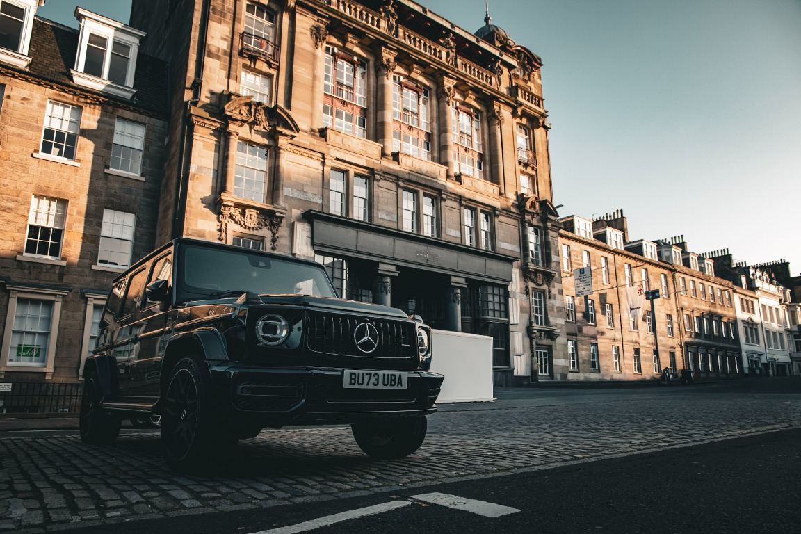 A black Mercedes parked on a historic city street in golden light.